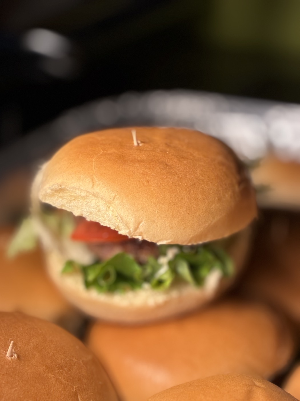 Mini hamburguesa con lechuga y jitomate sobre una charola de hamburguesas para evento