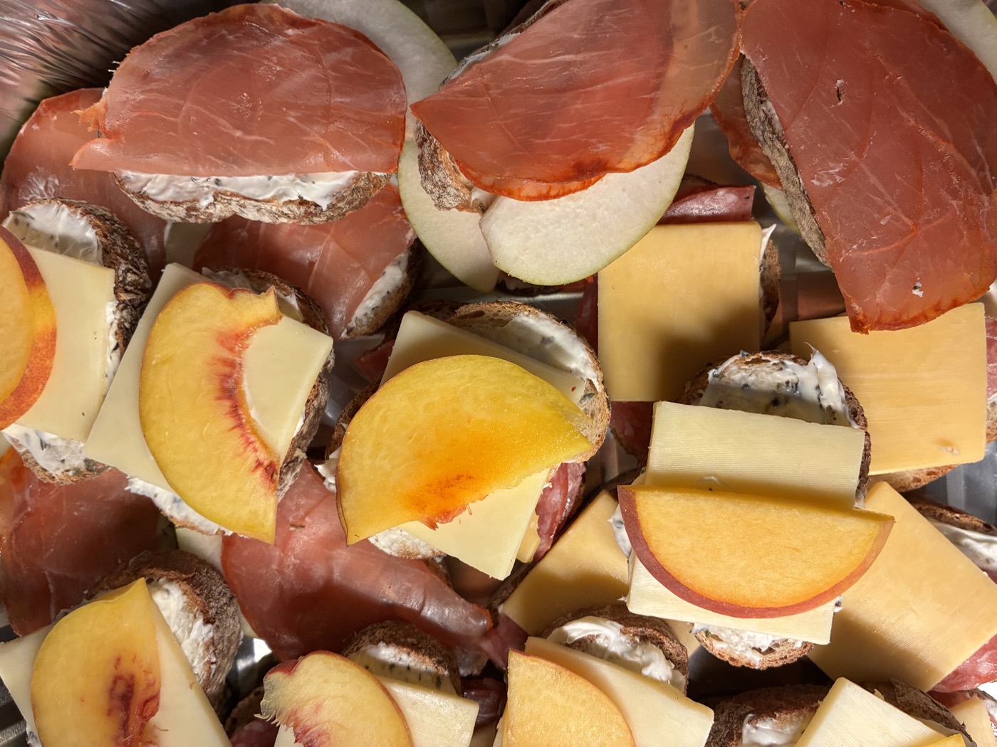 Tapas de pan con queso crema, jamón serrano, queso y rebanadas de durazno